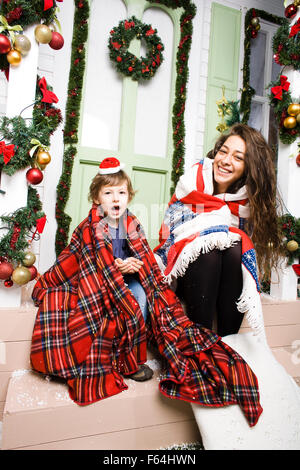 Famille heureuse à Noël de bonnets rouges en attente invités et souriant à l'extérieur chambre, frère et sœur hugging Banque D'Images