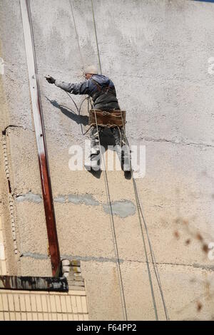 Peintre brave homme athlétique formulaire accrocher sur les cordes et brash le mur Banque D'Images