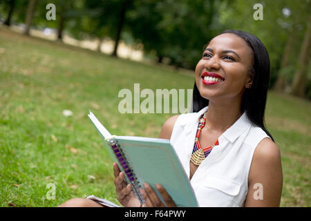 Young student sitting in the park holding son livre Banque D'Images