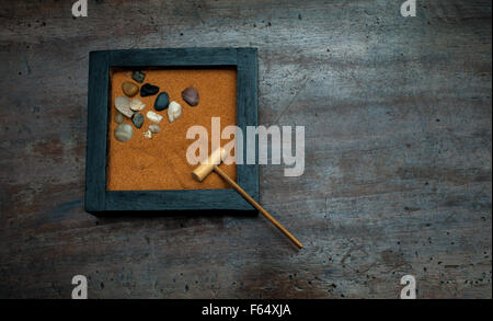 Jardin zen avec le râteau et pierres, sable orange sur de bois grattées Banque D'Images