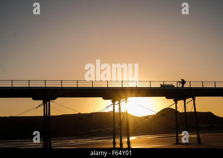 Un photographe s'aligne son tir alors que le soleil se lève sous la jetée victorienne à Saltburn-by-the-Sea en Angleterre, Royaume-Uni. Banque D'Images