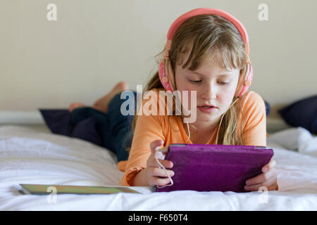 Fille de travailler sur iPad mini avec écouteurs rose Banque D'Images