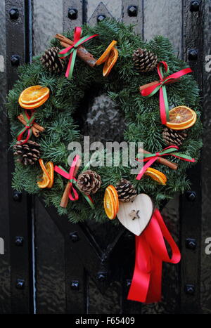 Une guirlande de noël, ou couronne, avec des tranches d'orange séchée et des bâtons de cannelle est suspendu à la porte en bois d'une maison Banque D'Images