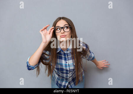 Portrait d'enquête intelligente jolie fille en chemise à carreaux avec des cheveux longs, dans les verres sur fond gris Banque D'Images