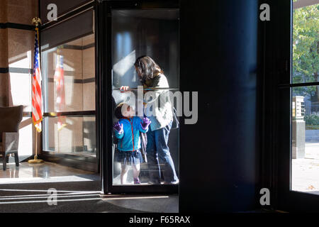 Une mère et son enfant en passant par une porte tournante qui mène à l'entrée d'un immeuble dans le sud de Manhattan, New York. Banque D'Images