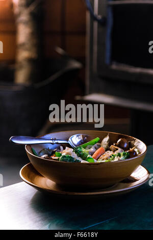 Vue de la soupe aux légumes ou ragoût dans une couleur brune ou tan bowl dans une plaque, sur un bleu verdâtre du grain du bois dans l'environnement rustique Banque D'Images