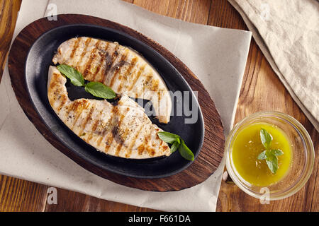 Espadon grillé dans une poêle en fonte sur une table en bois, garni de menthe, origan, sel et salmoriglio Banque D'Images
