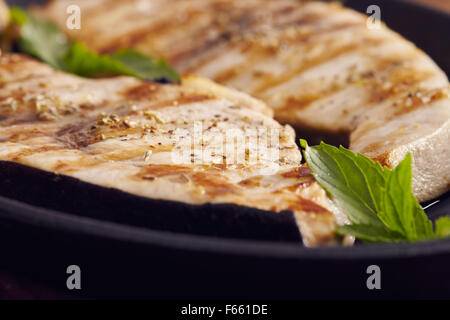 Espadon grillé dans une poêle en fonte sur une table en bois, garni de menthe, origan, sel et salmoriglio Banque D'Images