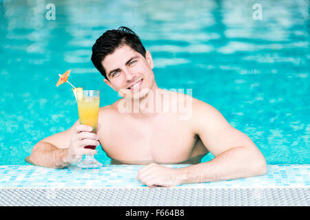 Beau jeune homme de boire un cocktail tout en vous relaxant dans une piscine Banque D'Images