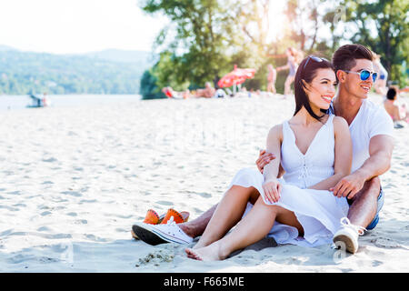 Couple amoureux assis à une plage de sable fin et souriant Banque D'Images