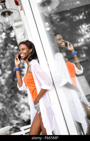 Belle black woman talking on phone and smiling durant une journée d'été et son reflet montrant sur la fenêtre Banque D'Images