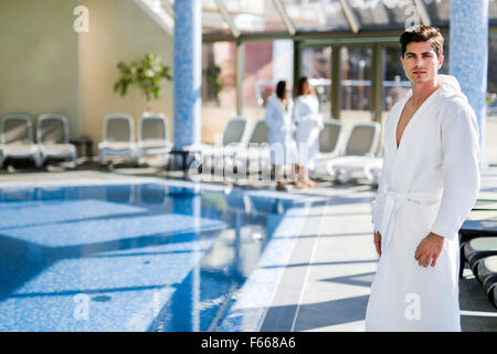 Homme debout à côté d'une piscine dans une robe et relaxant Banque D'Images