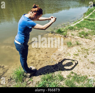 Young caucasian woman making heart shape avec ses mains sur le bord du lac. Banque D'Images