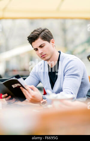 Beau jeune homme à la recherche, à l'aide du menu à l'extérieur Banque D'Images