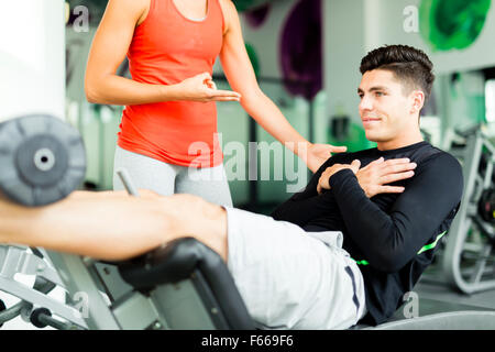 Belle jeune femme demandant à un jeune homme dans la salle de sport et d'entraînement sur son Banque D'Images