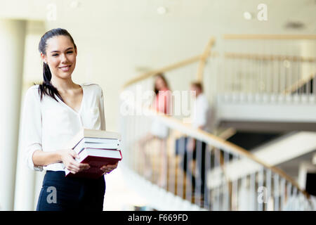 Belle femme holding books et souriant dans une bibliothèque moderne Banque D'Images