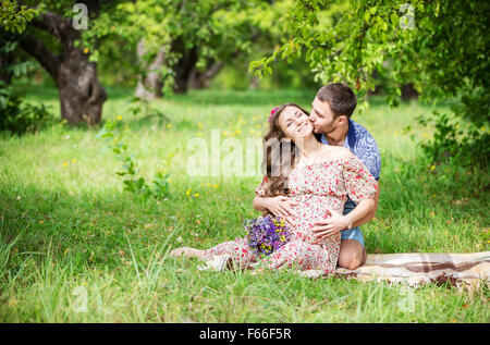 Happy young couple expecting baby sitting on Green grass Banque D'Images
