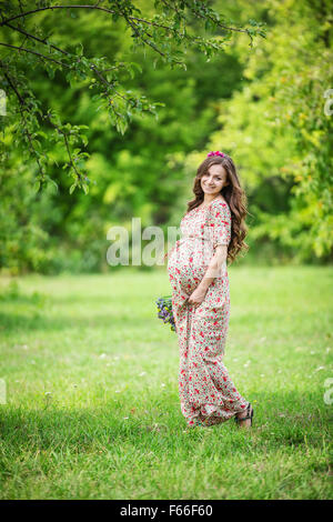 Belle femme enceinte portant des fleurs à l'extérieur dans le parc d'été Banque D'Images