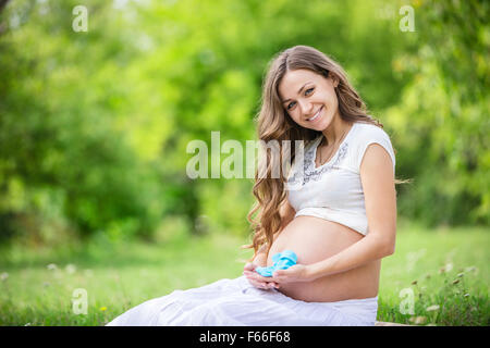 Beautiful pregnant woman holding baby booties et souriant à l'extérieur dans le parc Banque D'Images