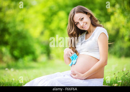Beautiful pregnant woman holding baby booties et souriant à l'extérieur dans le parc Banque D'Images