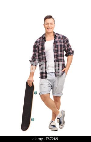 Portrait d'une jeune patineuse masculins s'appuyant sur son skateboard et regardant la caméra isolé sur fond blanc Banque D'Images