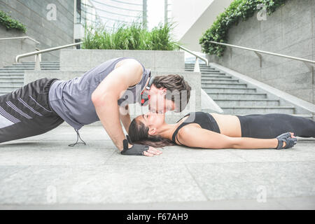 Couple de jeunes handsome young man and woman stretching sportif - il fait pousser ups s'embrasser sa petite amie, tant avec les yeux fermés - l'amour, le fitness, concept Banque D'Images