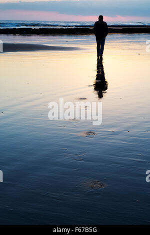 Homme marchant le long de la plage, laissant des traces de pas dans le sable à l'aube. Northumberland, Angleterre Banque D'Images
