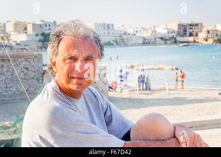 Souriant et bronzé middle-aged man détente en vacances, croisant ses bras devant le panorama à couper le souffle d'une ville côtière italienne Banque D'Images