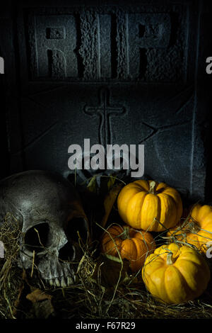 Une vie toujours inspiré de l'Halloween. Un crâne et des citrouilles assis dans les feuilles mortes en face d'une pierre tombale spooky . Banque D'Images