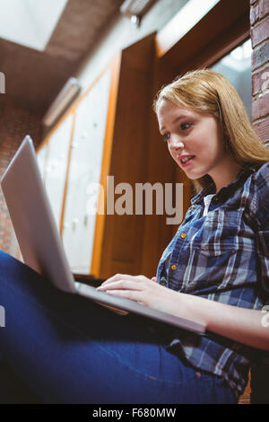 Étudiant porté assis sur le sol contre le mur à l'aide d'ordinateur portable Banque D'Images
