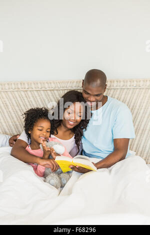 Joli couple avec sa fille lire un livre au lit Banque D'Images