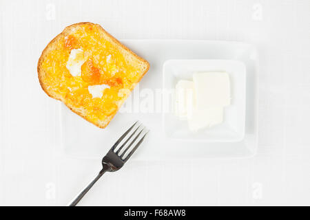 Pain doré avec propagation de l'orange amère en marmelade ou en confiture, beurre peel confits avec des boucles, fourchette et vaisselle sur nappe blanche Banque D'Images