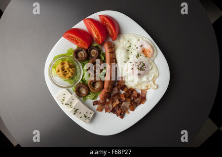 Petit-déjeuner servi sur une plaque blanche, oeufs, fromage, bacon, champignons, tomates Banque D'Images