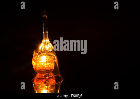 Cloche de verre ouvragé, bougie allumée à l'arrière isolé sur fond noir avec de multiples reflets de lumière et de réflexion miroir Banque D'Images