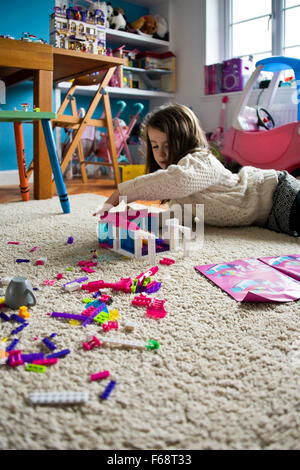 Portrait vertical d'une petite fille jouant avec des blocs de construction en plastique dans sa salle de jeux. Banque D'Images