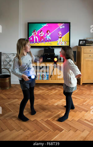 Portrait vertical de deux petites filles danser et chanter ensemble sur leur console de jeux. Banque D'Images