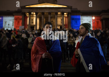 Deux hommes drapés dans des drapeaux français chanter la Marseillaise, l'hymne national français, en face de la Galerie nationale, allumé avec le Tricolore comme des milliers de personnes se rassemblent à Trafalgar Square, Londres, Royaume-Uni en solidarité avec le peuple français après les attentats à Paris, où au moins 130 personnes ont été tuées par une série d'attaques terroristes. Banque D'Images