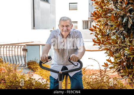 Personnes âgées de sexe masculin ne cesse de monter par l'octogénaire doing exercise bike sur le jardin de la maison Banque D'Images