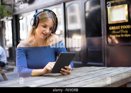 Jeune femme portant des écouteurs et de la lecture d'un livre électronique Banque D'Images