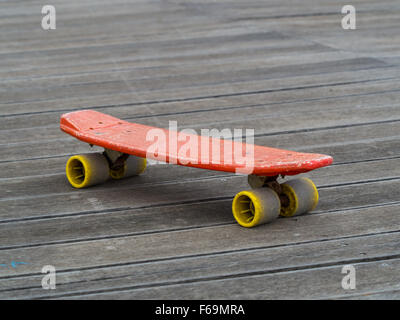 Ancien skate board en plastique rouge et jaune sur la surface en bois Banque D'Images