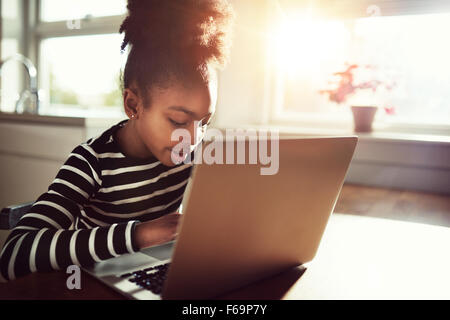 Jeune fille africaine elle-même amusant à la maison assis à la table à manger, la navigation internet sur un ordinateur portable Banque D'Images