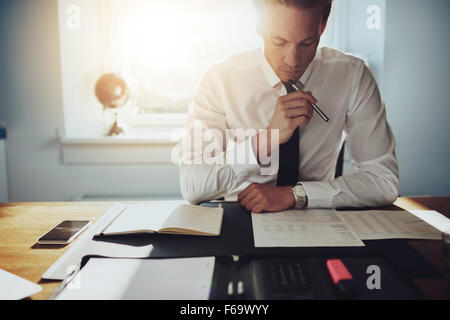 L'homme d'affaires sérieux travaillant sur des documents à la concentré avec porte-documents et téléphone sur la table Banque D'Images