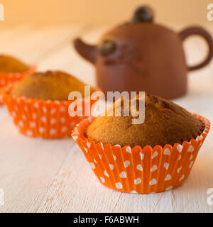 Muffins orange papier cupcake avec pois blancs et marron théière en céramique sur un fond en bois blanc, carré Banque D'Images