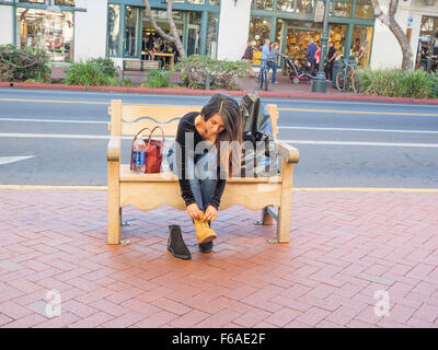 Une jeune femme adultes hispaniques modifications dans les nouvelles chaussures qu'elle vient d'acheter sur un banc public sur le trottoir de State Street en Banque D'Images