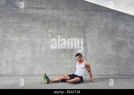 Homme sportif de remise en forme et stretching relaxant les muscles et les jambes portant un débardeur blanc, bien construire, copy space Banque D'Images