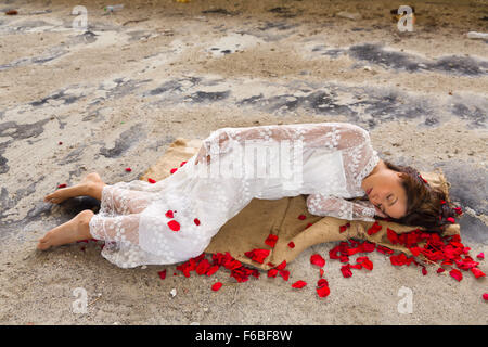 Belle jeune femme en robe de dentelles anciennes dormir dans un bâtiment abandonné de pétales de rose Banque D'Images