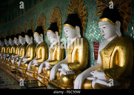 SAGAING, Myanmar — debout sur une colline à Sagaing, la pagode OoHminThoneSel présente une longue alcôve incurvée bordée de dizaines de statues du Bouddha. Après de récentes rénovations et améliorations en cours rendues possibles par des donateurs, la pagode est richement décorée avec des mosaïques de carreaux colorés et de la peinture fraîche et brillante. Banque D'Images