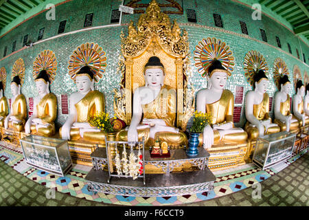 SAGAING, Myanmar — debout sur une colline à Sagaing, la pagode OoHminThoneSel présente une longue alcôve incurvée bordée de dizaines de statues du Bouddha. Après de récentes rénovations et améliorations en cours rendues possibles par des donateurs, la pagode est richement décorée avec des mosaïques de carreaux colorés et de la peinture fraîche et brillante. Banque D'Images