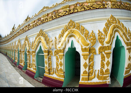 SAGAING, Myanmar — debout sur une colline à Sagaing, la pagode OoHminThoneSel présente une longue alcôve incurvée bordée de dizaines de statues du Bouddha. Après de récentes rénovations et améliorations en cours rendues possibles par des donateurs, la pagode est richement décorée avec des mosaïques de carreaux colorés et de la peinture fraîche et brillante. Banque D'Images