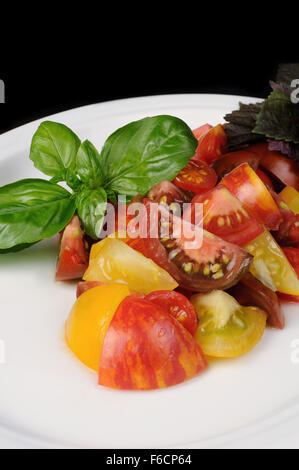 Tranches de différentes variétés de tomates avec basilic sur une plaque Banque D'Images